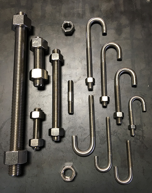 Assorted stainless steel U-bolts and threaded rods with nuts arranged on a metal surface &ndash; durable industrial fasteners for construction and pipe support.